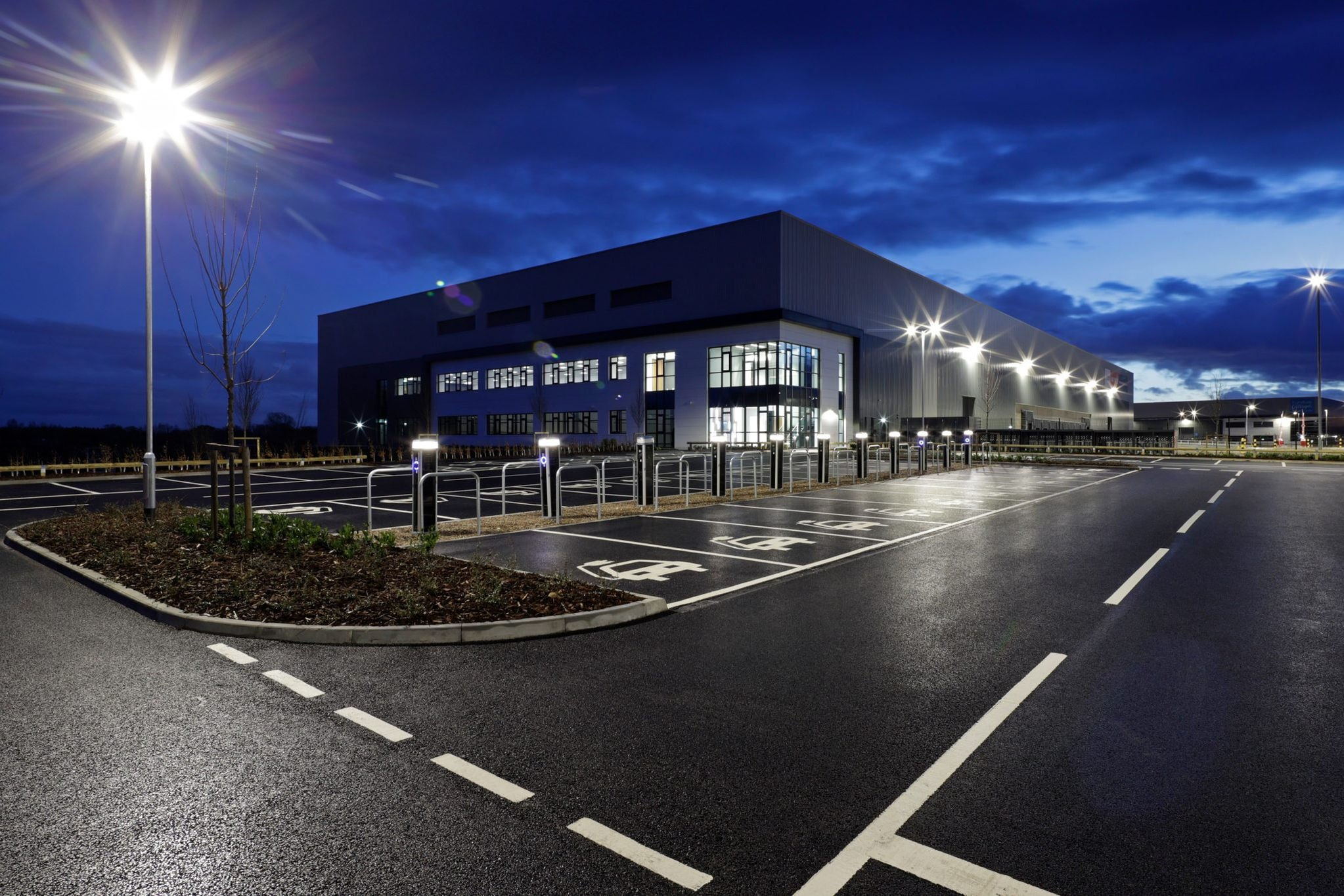 Lit EV charging bays outside a commercial building at dusk